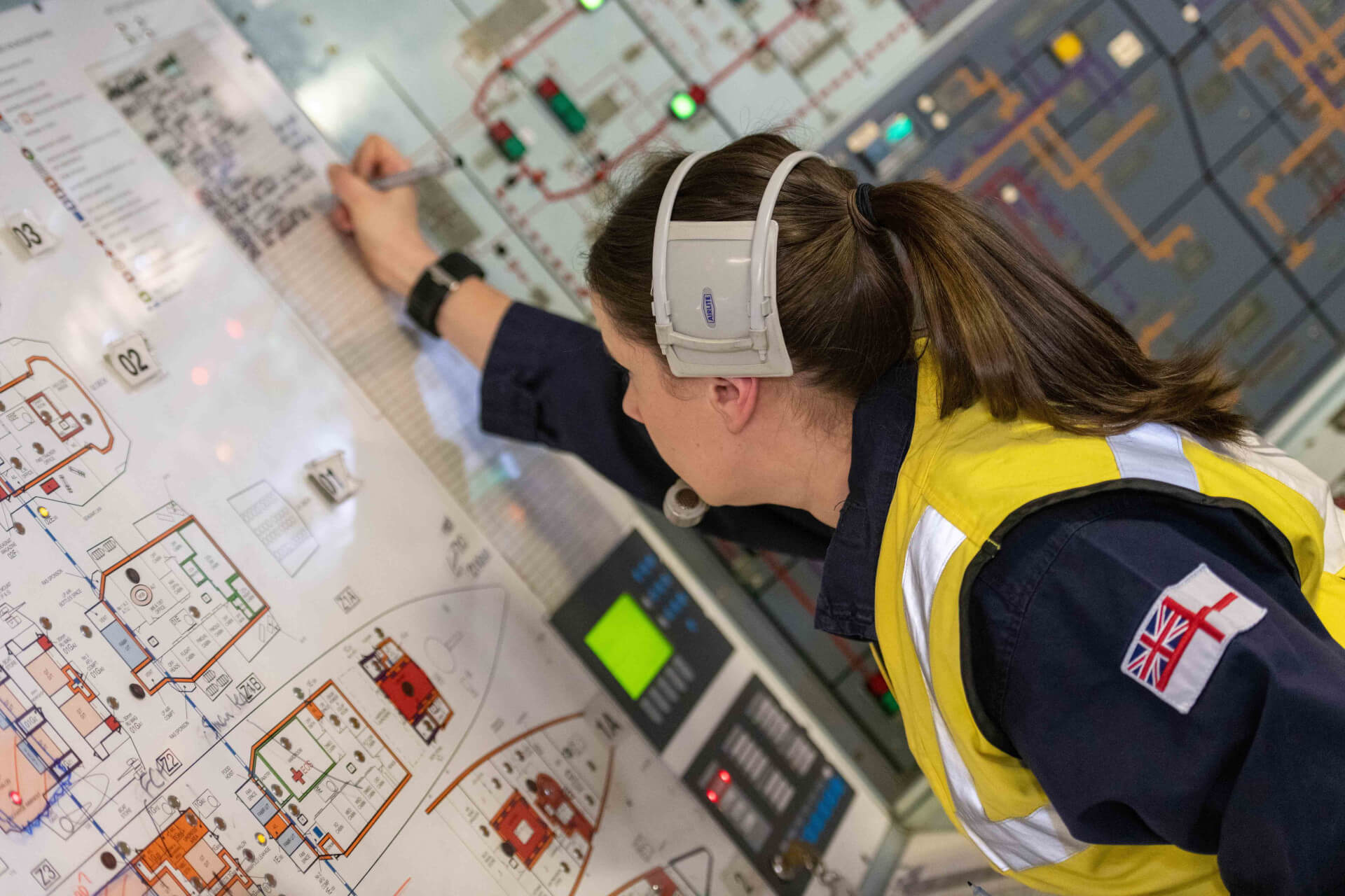 Female Royal Navy Technician working on Ships board, wearing a yellow high-vis jacket